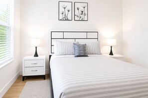 A neatly arranged bedroom with a bed, two bedside tables, and a window with blinds. - Prime Suite by Convention Center and Bathhouse Row (Hot Springs)