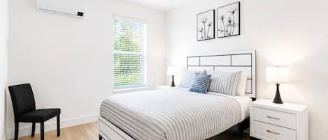 A bedroom with a bed, bedside tables, a chair, a window with blinds, and wall art.
