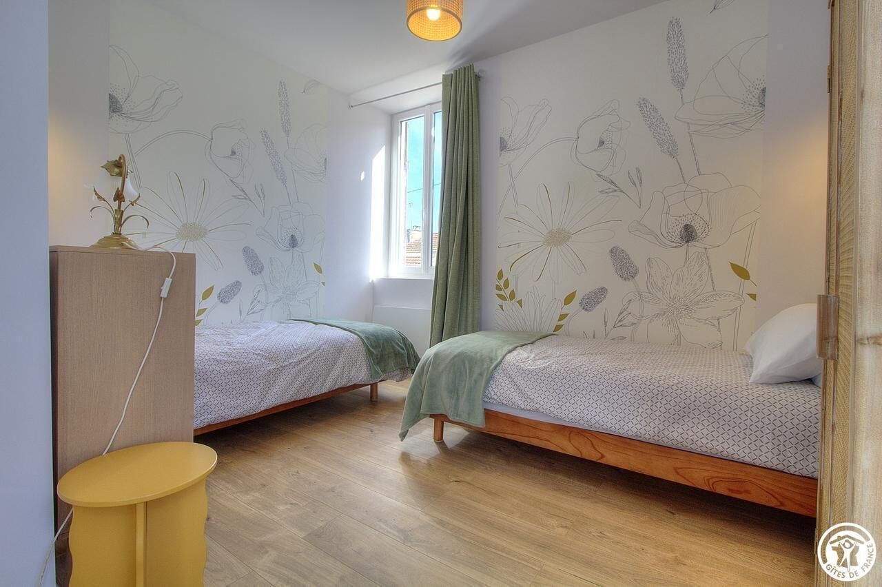 A bedroom with two beds, a small table, a lamp, and a window with curtains.