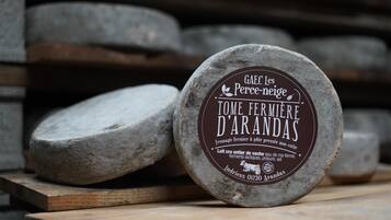 A round cheese wheel with a label, placed on a wooden surface with other cheese wheels in the background.