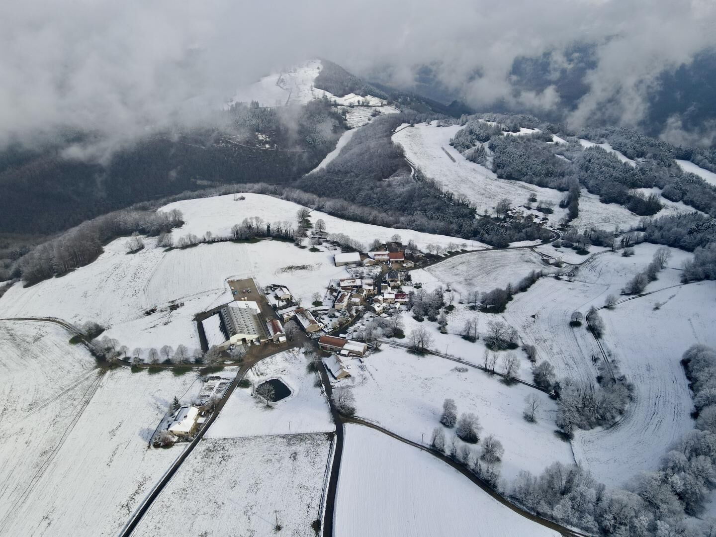 An aerial view of a snow-covered village with buildings, roads, and a mountain in the background.