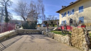 A gravel driveway leading to a stone wall and a building with blue shutters.