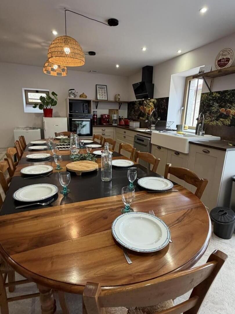 A dining area with a wooden table set for six, surrounded by chairs. A woven pendant light hangs above the table.