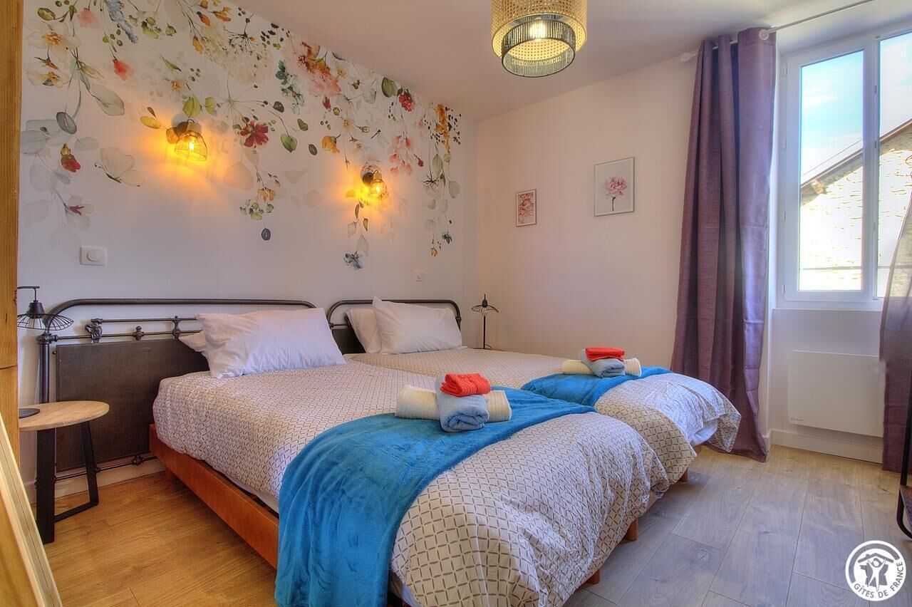 Camera da letto con due letti, una lampada a parete, una finestra con tende e un tavolino.
