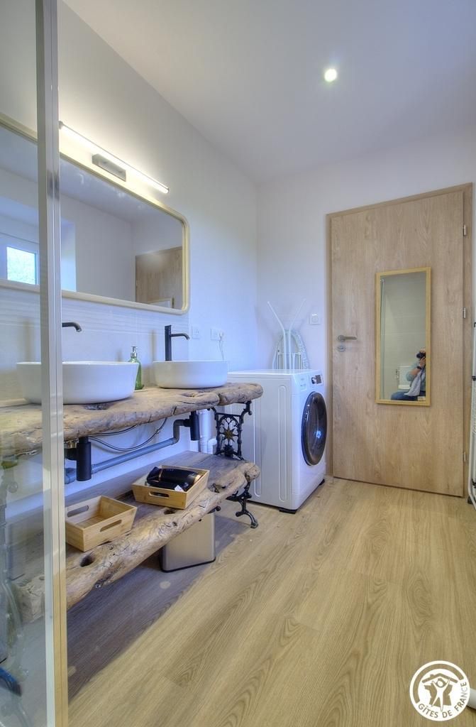 A modern bathroom with a wooden vanity, two sinks, a washing machine, and a mirror.