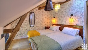A bedroom with a sloped ceiling, floral wallpaper, a wooden headboard, and two wall-mounted lamps.