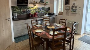 A dining area with a round table set for four, a kitchen with a stove, sink, and various appliances, and a window with blinds.