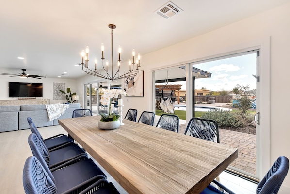 A modern dining area with a wooden table, black chairs, and a chandelier. - Spacious 5-bedroom house with Pickleball, Heated Pool, Hot Tub, and much more (Scottsdale)