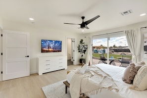 A bedroom with a bed, a ceiling fan, a TV, a plant, and a view of the outdoors. - Spacious 5-bedroom house with Pickleball, Heated Pool, Hot Tub, and much more (Scottsdale)