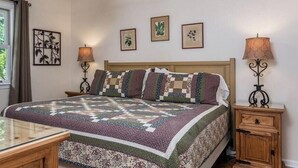 Un dormitorio con una cama grande, una mesita de noche, cortinas en una ventana y decoración en la pared.