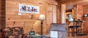 Ein Holzhütten-Interieur mit Essbereich, einer Couch, einer Lampe und einem gerahmten Bild an der Wand.
