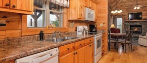 Une cuisine de style rustique, avec des murs en bois, des comptoirs en granit, un four à micro-ondes, une cuisinière et un coin repas agrémenté d’une cheminée.