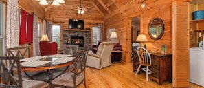 L’intérieur chaleureux d’un chalet comprend une table à manger, des chaises, une cheminée, un téléviseur et un coin cuisine.