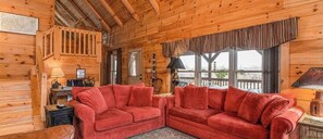 Ein gemütliches Blockhaus-Interieur mit einem roten Sofa, Holzwänden, einem Fenster mit Aussicht und einer Lampe auf einem Tisch.