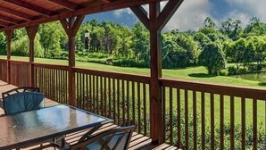 A covered outdoor deck with a table and chairs, a grill, and a view of a green landscape. - Barkwells Asheville Libby Cabin: Dog-Centric Resort, Hot Tub, Pond, Fenced Yard! (Mills River)