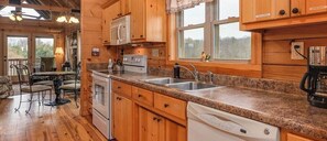 Eine hölzerne Küchenzeile im Chalet-Stil mit Granit-Arbeitsplatten, einem Geschirrspüler, einem Herd und einer Spüle.