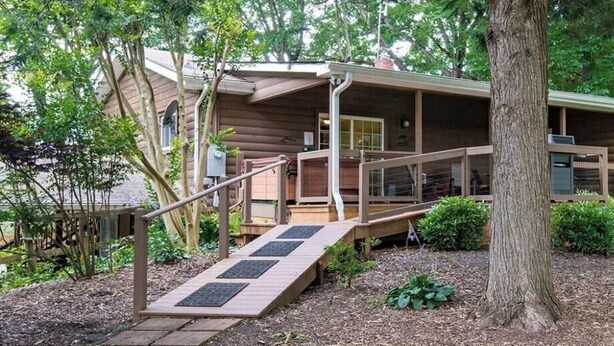 Une cabane avec une façade en bois, une véranda et une rampe menant à l’entrée.
