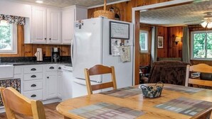 L’intérieur chaleureux d’un chalet avec une table à manger en bois, des chaises, un réfrigérateur et un canapé.