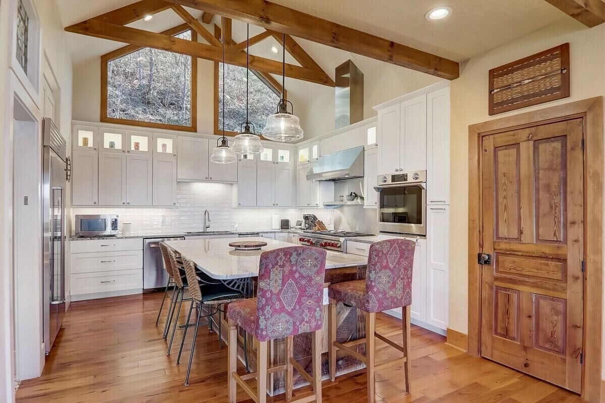 A modern kitchen with white cabinets, a large island, hanging pendant lights, and a wooden ceiling.