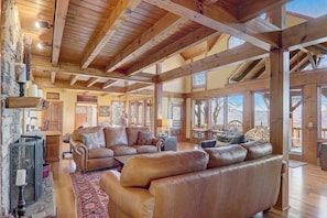 Ein geräumiges Wohnzimmer mit Ledersofas, einem Steinkamin und großen Fenstern mit Blick ins Freie.