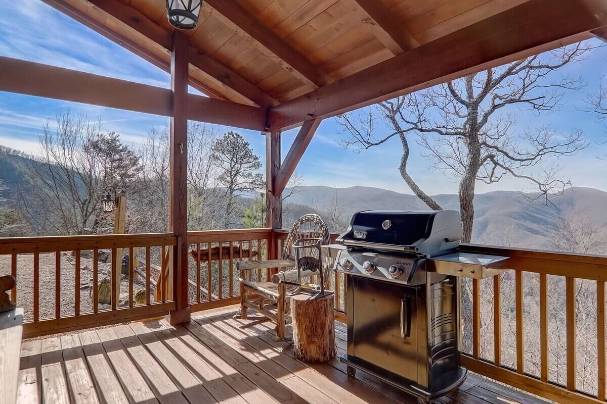 Une terrasse en bois avec un barbecue et des chaises, offrant une vue sur un paysage montagneux.