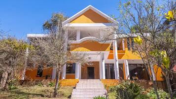 A two-story building with a yellow facade and white trim, featuring a central entrance with steps and a small porch area.