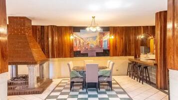 A dining area with a brick fireplace, wooden paneling, a checkered floor, and a bar with stools.