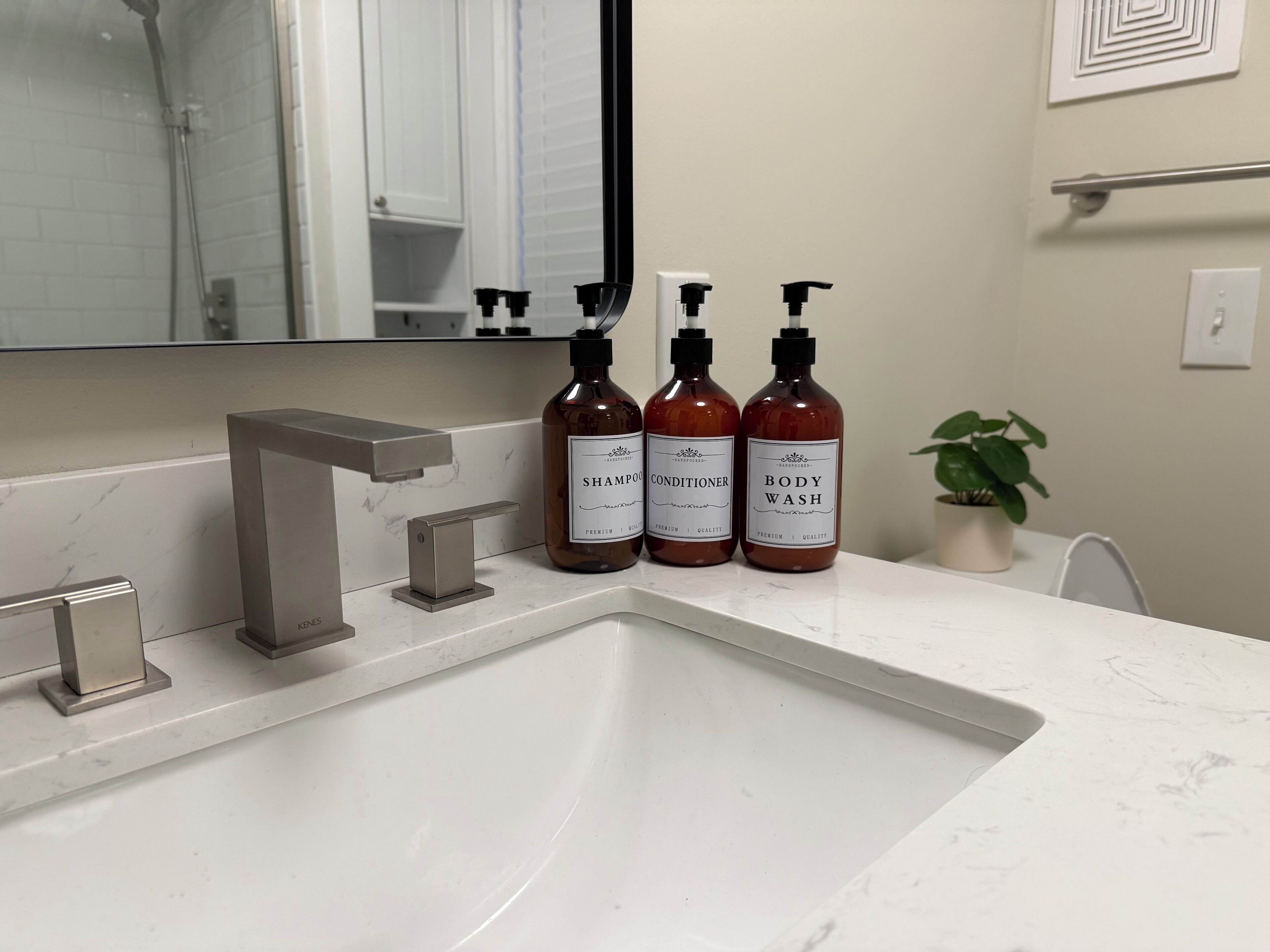 Une salle de bain avec un lavabo blanc, un robinet moderne et trois bouteilles de gel douche, d’après-shampoing et de shampoing.