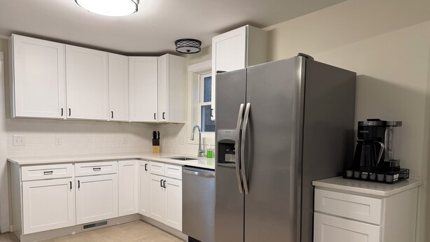 A modern kitchen with white cabinets, a stainless steel refrigerator, a built-in dishwasher, and a coffee maker on the countertop.