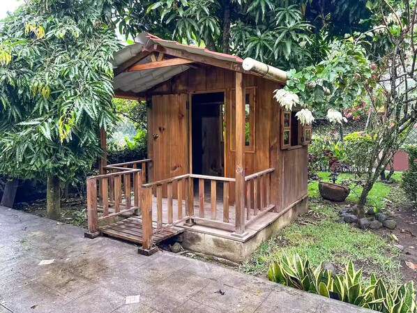 A small wooden structure with a porch, surrounded by lush greenery.
