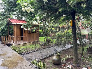 A wooden structure with a red roof, surrounded by lush greenery and a stone pathway.