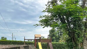 A playground with a slide and a wooden structure, surrounded by greenery and a hedge. - Casa Familiar ubicada a minutos de Xetulul (Guatemala)