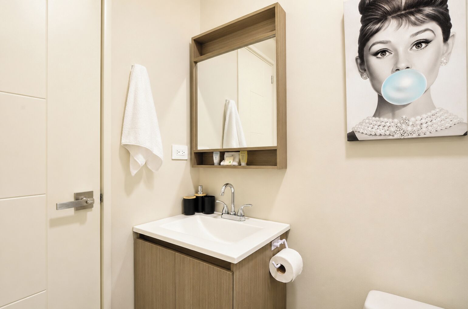 Une salle de bain avec un lavabo, un miroir, une serviette, du papier toilette et un tableau accroché au mur.