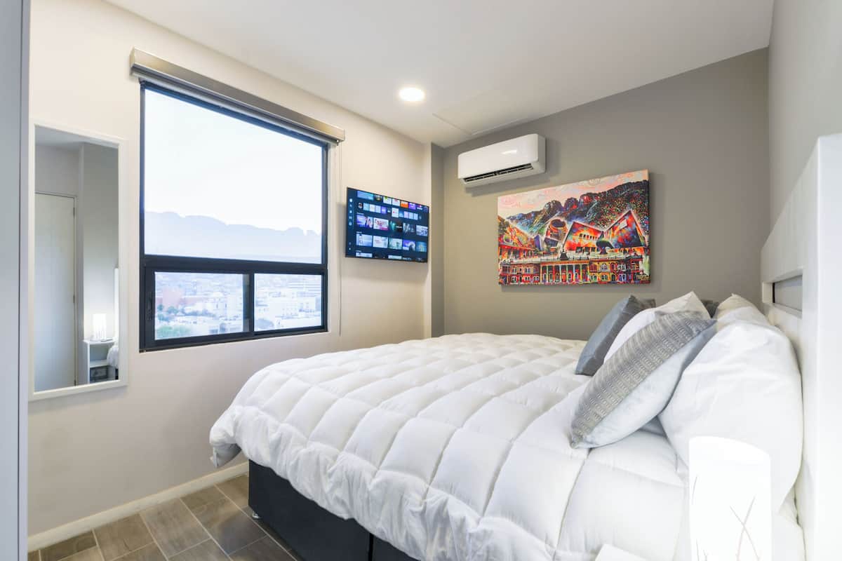 A bedroom with a large bed, a TV mounted on the wall, and a window with a view.