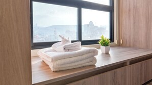 Een uitzicht op een stadsgezicht vanuit een raam, een stapel witte handdoeken en een kleine potplant op een houten plank.