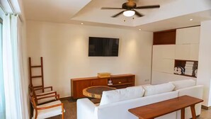 Ein modernes Wohnzimmer mit einer Couch, einem Holztisch, einem an der Wand montierten Fernseher und einem Deckenventilator.