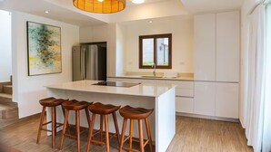 Eine moderne Küche mit Kochinsel, Barhocker, Edelstahlgeräten und einem großen Fenster.