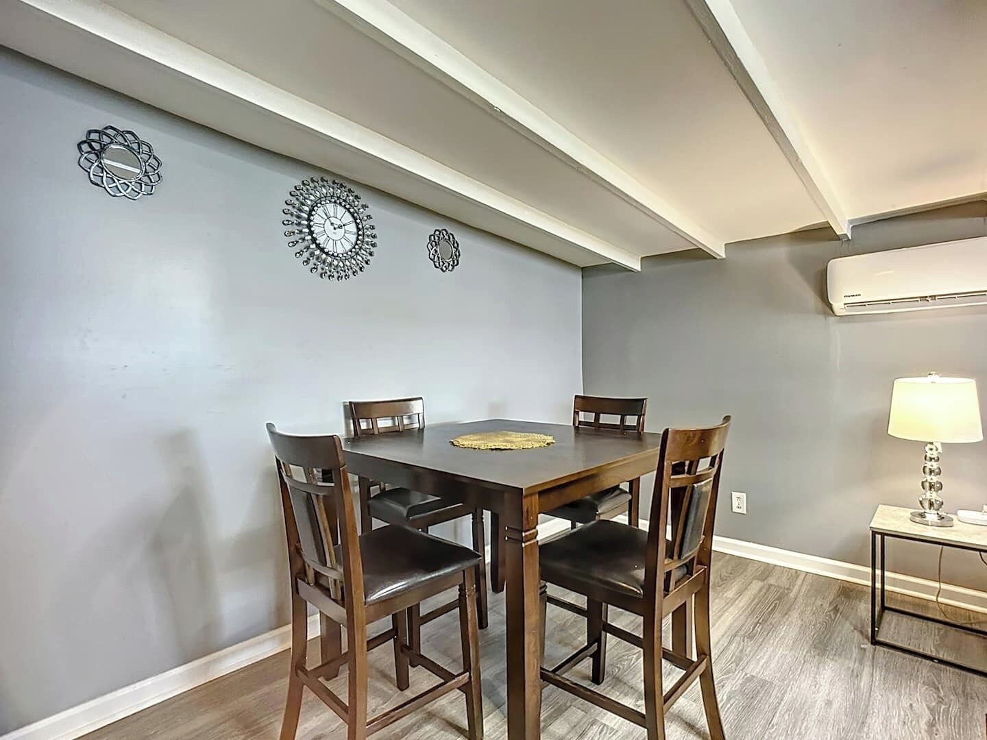 Un espace repas comprenant une table et des chaises en bois, des éléments décoratifs muraux et un appareil de climatisation.