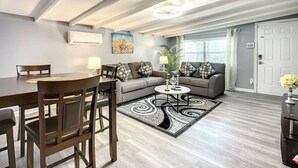 A modern living room with a dining area, a grey sofa set, a coffee table, and a patterned rug.