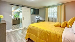 A bedroom with a bed, a desk, a TV, and a sliding door leading to another room.