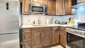 A modern kitchen with wooden cabinets, a stainless steel refrigerator, a microwave, a sink, a toaster, and an oven.