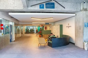 Zona de recepción con espacio para sentarse, mostrador de recepción y pared con diseño de pequeños cuadrados.