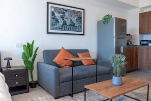 Una sala moderna con un sofá gris, cojines naranjas, una mesita, una planta en maceta y un mapa mundial enmarcado en la pared.