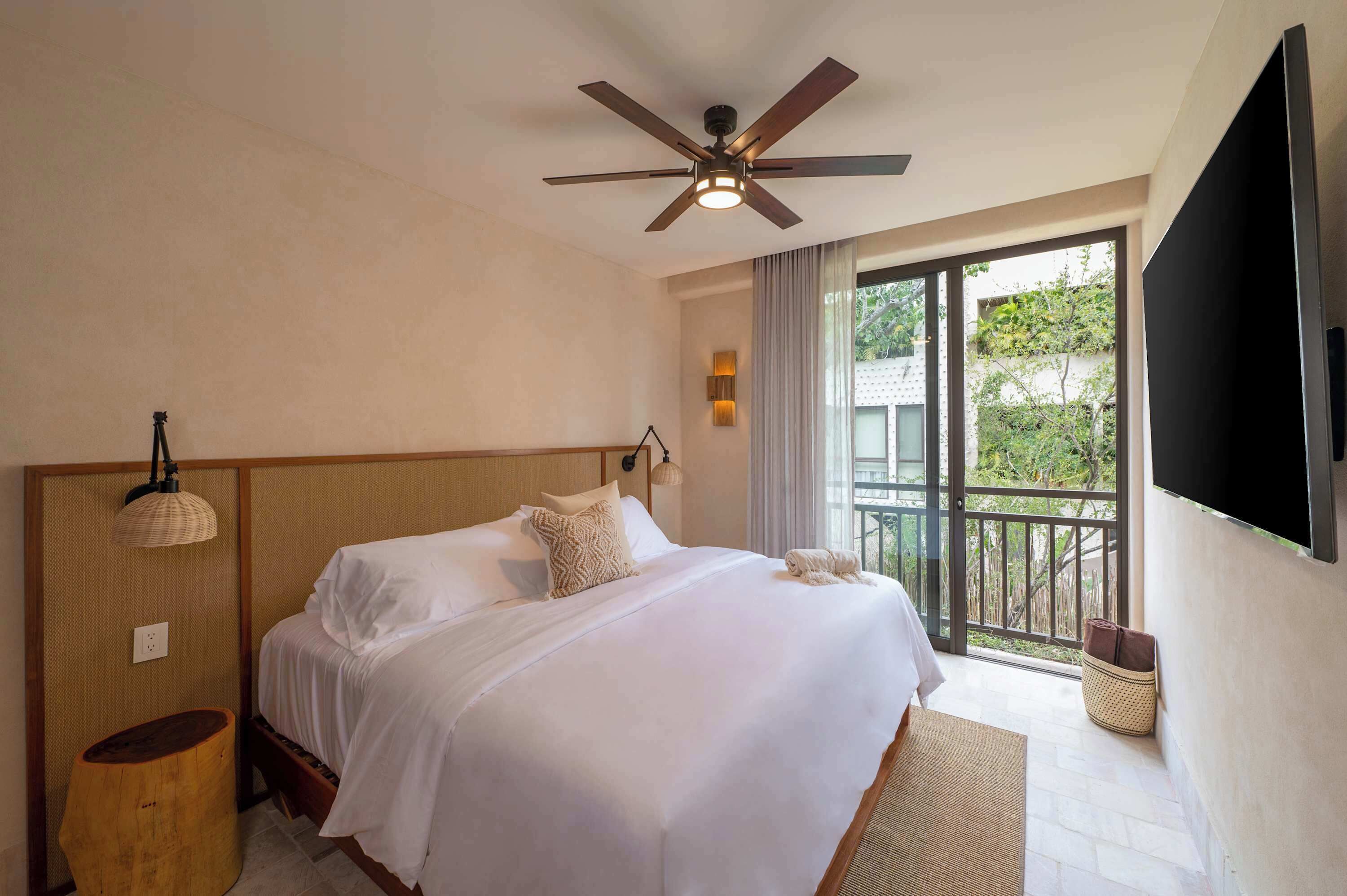 A bedroom with a bed, ceiling fan, and a view of the outdoors through a sliding glass door.