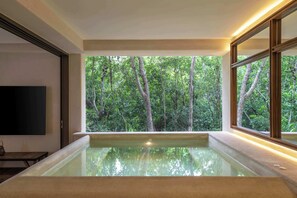 Ein modernes Badezimmer mit einer großen Badewanne, einem Flachbildfernseher und Blick auf einen Wald durch große Fenster.