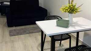 Ein modernes Wohnzimmer mit einem dunklen Sofa, einem weißen Esstisch mit zwei Stühlen und einer Vase mit gelben Blumen.