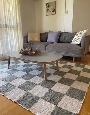 Un salon avec un tapis à carreaux, un canapé gris agrémenté de coussins et un tableau accroché au mur.