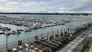 A marina with numerous boats docked, a pedestrian walkway, and outdoor seating with umbrellas. - Grand appartement avec jolie vue sur le port de St Cast, 3 chambres pour 6 personnes (ST CAST LE GUILDO)