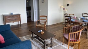 A living room with a sofa, a coffee table, and a dining area with chairs and a table set for four. - Grand appartement avec jolie vue sur le port de St Cast, 3 chambres pour 6 personnes (ST CAST LE GUILDO)