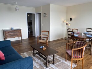 A living room with a sofa, a coffee table, and a dining area with chairs and a table set for four. - Grand appartement avec jolie vue sur le port de St Cast, 3 chambres pour 6 personnes (ST CAST LE GUILDO)
